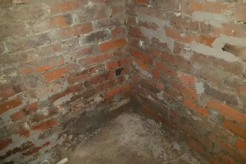 Narożnik piwnicy z ceglanymi ścianami, widoczne ślady prac związanych z hydroizolacją piwnicy od wewnątrz.