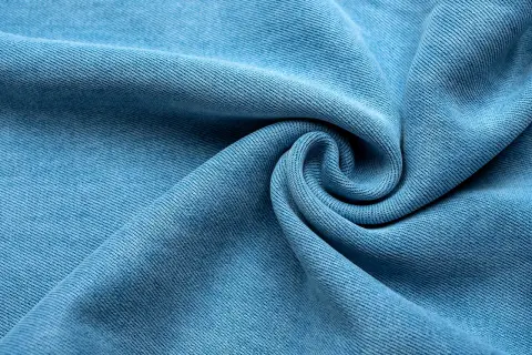 Miękka, błękitna tkanina lyocellu z charakterystycznym splotem, ułożona w eleganckie fale i spiralę.