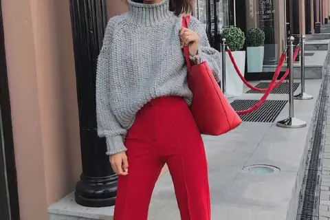 Chaqueta de punto gris y pantalones granate combinan a la perfección. Un bolso rojo vibrante completa el look.