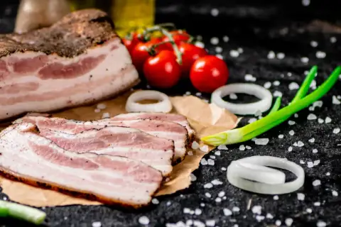 Idealny boczek do carbonary: plastry wędzonego boczku, pomidorki, cebula i szczypiorek na czarnym tle.