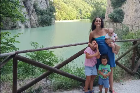 Famiglia felice nella golena del Furlo, con un lago turchese e montagne verdi sullo sfondo.