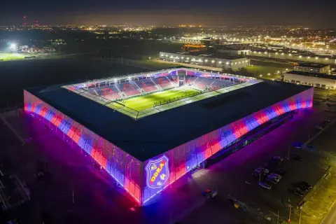 Nowoczesny stadion Odra Opole nocą, oświetlony kolorowymi światłami. Widać boisko i trybuny.