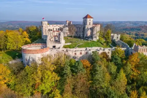 Ruiny zamków Orlich Gniazd na wzgórzu, otoczone jesiennym lasem. Polska flaga powiewa na wieży.