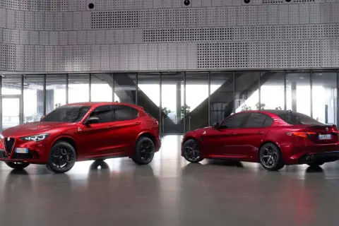 Dwa czerwone Alfa Romeo, SUV Stelvio i sedan Giulia Quadrifoglio, stoją obok siebie w nowoczesnym wnętrzu.