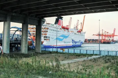 Widok na prom Stena Line w Gdyni, z dwoma mężczyznami na pierwszym planie. W tle portowe dźwigi i inne statki.