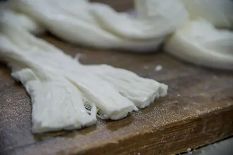 Formaggio a pasta filata, lavorato a mano, con fili bianchi e morbidi su un tagliere di legno.