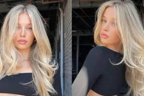 Blond włosy z subtelnym scandi hairline, falowane i pełne objętości, opadają na ramiona.