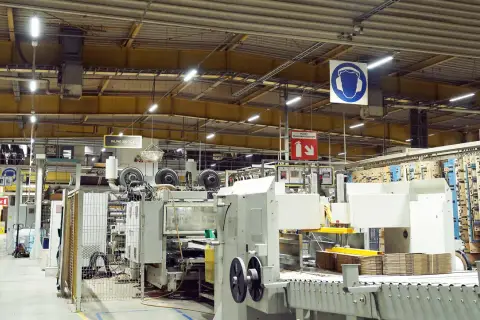 Jasne, oto opis:

Nowoczesne oświetlenie hali magazynowej zapewnia widoczność maszyn produkcyjnych i stosów kartonów.