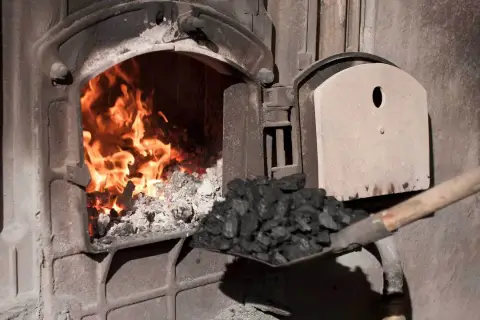Fachowiec od pieca zasypuje węglem palenisko, gdzie szaleje ogień.