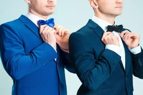 Dwóch mężczyzn w granatowych garniturach poprawia muszki. Jeden w niebieskiej, drugi w czarnej. Jaka mucha do granatowego garnituru?