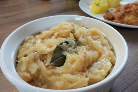 Pyszna kapusta kiszona zasmażana z liściem laurowym i zielem angielskim, podana w białej miseczce.