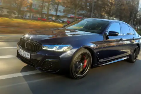 Ciemnoniebieskie BMW 540d sunie po drodze, odbijając jesienne słońce.