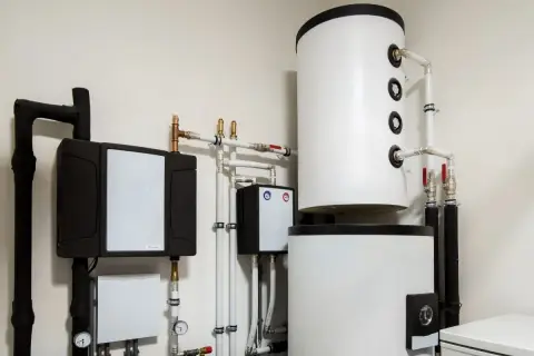 Instalacja pompy ciepła z zasobnikami i rurami. Widoczny panel sterowania, który może wpływać na histerezę pompy ciepła, zapewniając optymalną pracę systemu.