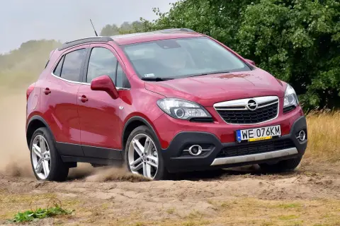 Czerwony Opel Mokka 1.4 Turbo z napędem na cztery koła pokonuje piaszczysty teren, wzbijając tumany kurzu.