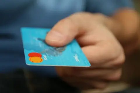 Main tenant une carte bancaire bleue, prêt à effectuer un achat. Il est possible de bloquer un paiement CB en cas de perte.