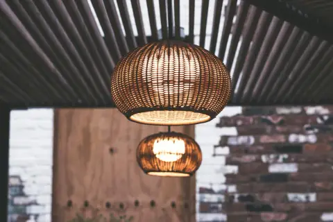 Dos lámparas de mimbre esféricas cuelgan bajo un techo de listones. La luz cálida que emiten crea un ambiente acogedor, con unos agradables lúmenes por m2.