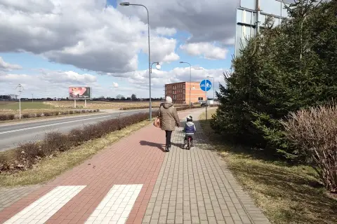 Kobieta z dzieckiem na rowerze idzie chodnikiem. Długość kolumny pieszych nie może przekraczać, ale tu jest tylko dwójka.
