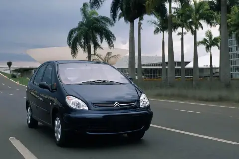 Ciemnoniebieski Citroen Xsara Picasso jedzie drogą wśród palm, w tle nowoczesna architektura.