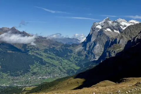 Panoramic view of a valley village nestled among green hills, with dramatic, snow-capped peaks of the Swiss Alps in the background. This scene exemplifies the best hikes in Swiss Alps.