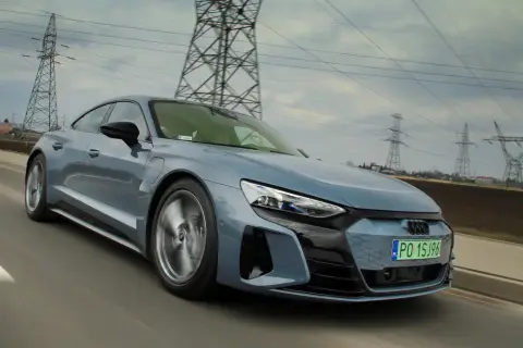 Szary Audi e-tron GT pędzi po drodze, otoczony liniami energetycznymi i słupami wysokiego napięcia.
