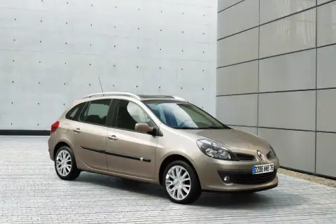 Beżowe Clio 3 kombi stoi na tle nowoczesnego budynku z betonową i metalową elewacją.