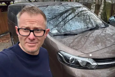 Mężczyzna w okularach przed brązowym vanem, gotowy do podpisania umowy komisu.