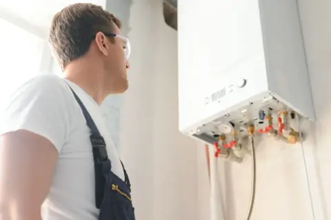 Technik w okularach ochronnych sprawdza instalację gazową. Wykonuje odpowietrzanie pieca gazowego, dbając o jego prawidłowe działanie.