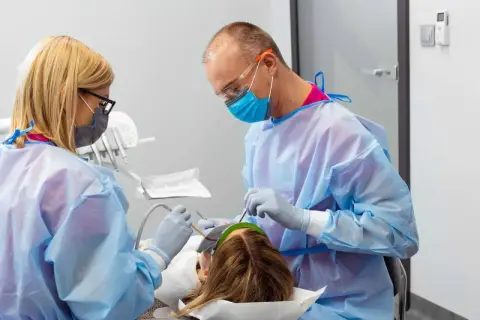 Znieczulenie u dentysty w ciąży. Dwoje stomatologów w fartuchach i maskach wykonuje zabieg u pacjentki.