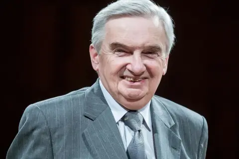 Uśmiechnięty starszy pan w szarym garniturze. Trudno zgadnąć, ile lat ma sznuk, ale wygląda na doświadczonego i życzliwego.