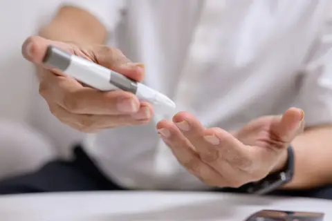 Osoba wykonuje badanie kodu metabolicznego, używając glukometru do nakłucia palca.