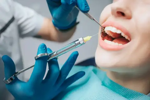 Dentysta podaje znieczulenie. Czy znieczulenie u dentysty boli? Pacjentka ma otwarte usta, a w nich widać igłę strzykawki.