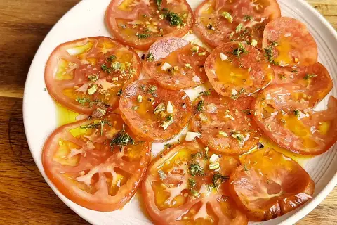 Carpaccio de tomate fresco con aceite de oliva, ajo picado y hierbas aromáticas. Un plato ligero y lleno de sabor.