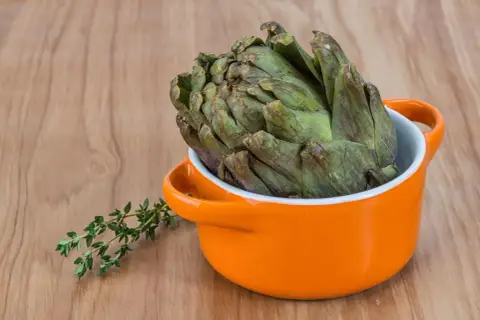 Un gros artichaut vert prêt pour la cuisson Cookeo, avec une branche de thym frais à côté.