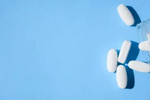 Białe tabletki, w tym oxycodone, wysypują się z przezroczystego pojemnika na niebieskim tle.