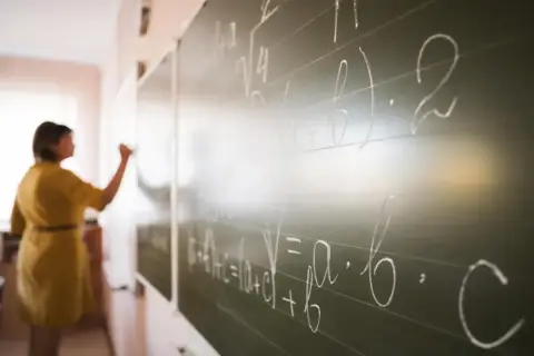 Nauczycielka pisze wzory matematyczne na tablicy. To jak art 20 kn, gdzie każdy symbol ma swoje znaczenie.