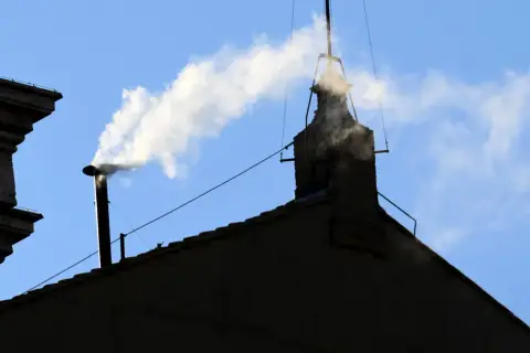Biały dym z komina na tle błękitnego nieba, jakby papież ogłaszał wybór.