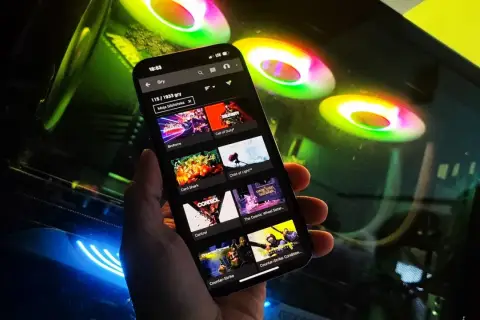 Przeglądanie listy gier na GeForce Now na telefonie, w tle świecące wentylatory komputera.