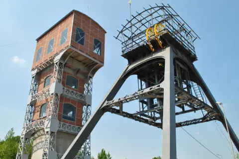 Dwie wieże kopalniane, jedna ceglana, druga metalowa z kołem, tworzą futurystyczny grawitacyjny magazyn energii.