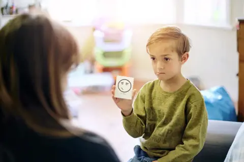 Chłopiec trzyma kartkę z rysunkiem smutnej buźki i napisem "SORRY".