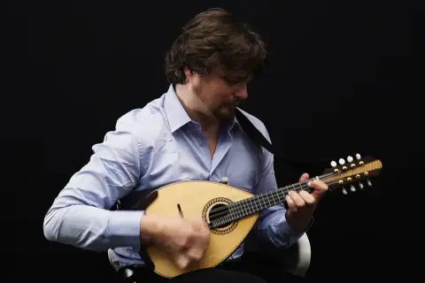 Un homme joue de la mandoline, son visage concentré sur l'instrument. Le son mélodieux de la mandoline emplit la pièce.