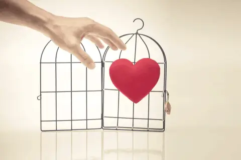 Mano che apre una gabbia con un cuore rosso dentro. Abbiamo fatto l'amore e non si fa sentire, il mio cuore è libero ma solo.