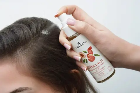 Dłoń aplikuje wcierkę do skóry głowy, by sprawdzić, czy wcierki do włosów działają. Włosy są ciemne, a produkt w sprayu.