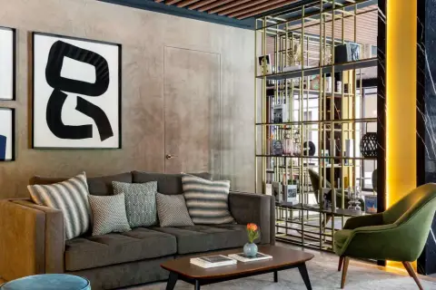 Sofá gris con cojines decorativos, mesa de centro y estantería dorada en un lobby de Radisson Collection.