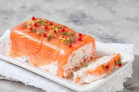 Une délicieuse terrine de saumon, garnie d'aneth, de baies roses et de zeste de citron, prête à être dégustée.