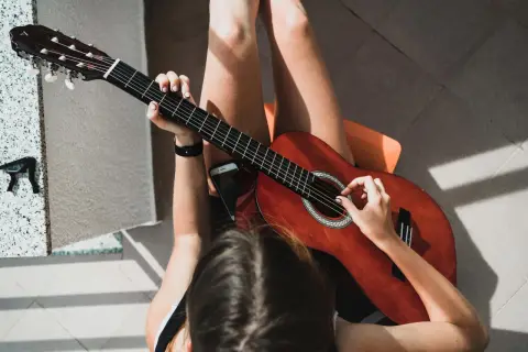 Dziewczyna gra na gitarze, jej palce tworzą akord g. Słońce rzuca ciekawe cienie.