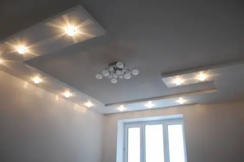 Nowoczesny sufit z wieloma punktami świetlnymi, tworzącymi rozproszone światło. Centralnie umieszczony designerski żyrandol.