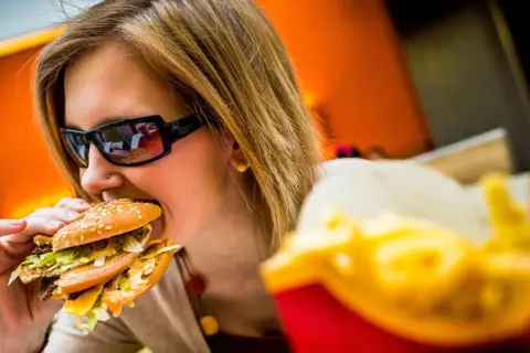 Dziewczyna w okularach je pysznego mcmuffin wieprzowy z jajkiem. Obok frytki.