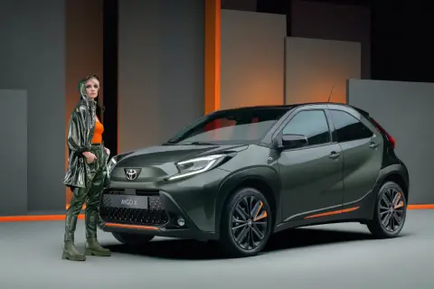 Stylowa kobieta obok zielonego Toyota Aygo X. Wiele osób szuka pozytywnych toyota aygo opinie, ten model wygląda obiecująco.