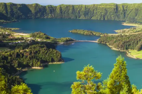 Malowniczy krajobraz portugalskiego archipelagu na Atlantyku: jezioro w kraterze wulkanicznym, otoczone zielonymi wzgórzami i niewielką wioską.