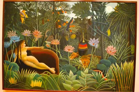 A woman reclines in a lush jungle, surrounded by exotic flowers and watchful lions. This is a classic example of Henri Rousseau's jungle paintings, filled with vibrant colors and a dreamlike atmosphere.